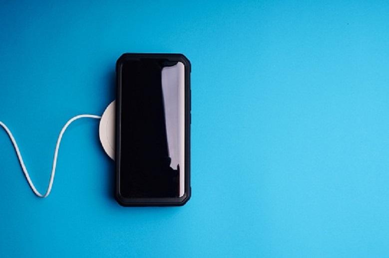 Wireless charging dock and smartphone on blue background.