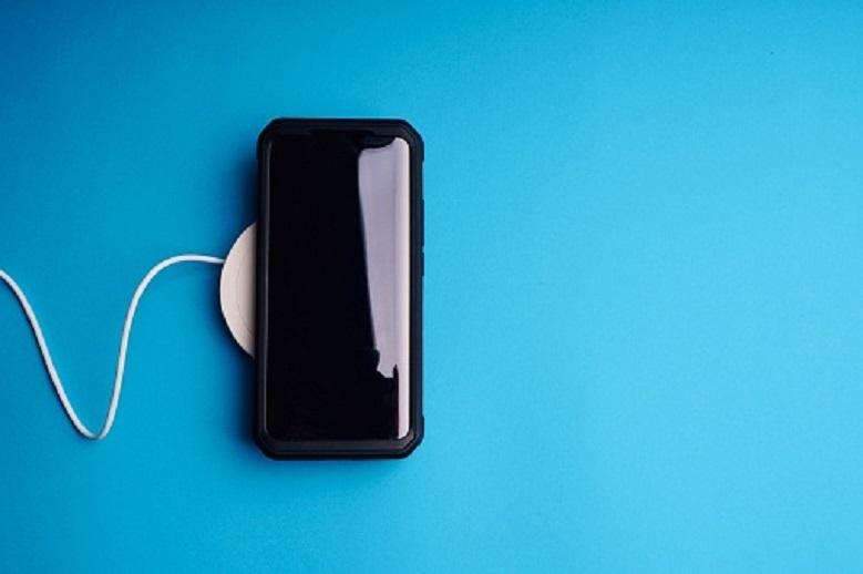 Wireless charging dock and smartphone on blue background.