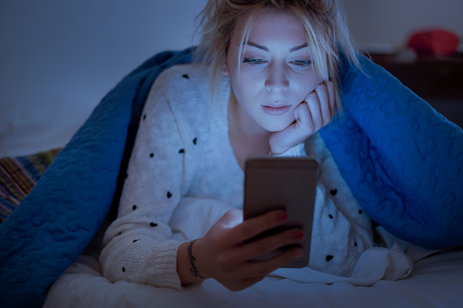 Woman holding mobile phone while laying on bed at night
