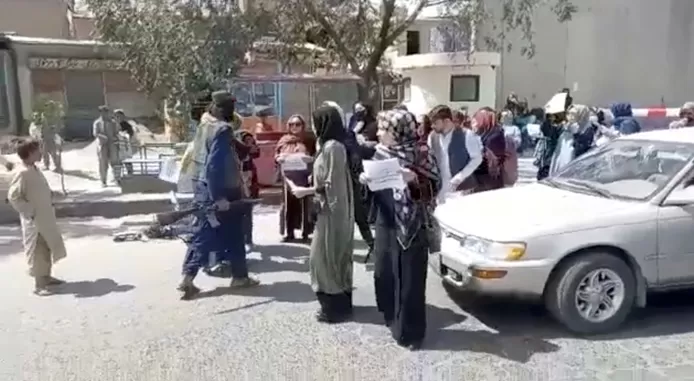 A still from a video shows an armed Taliban fighter stepping towards a group of protesting women
