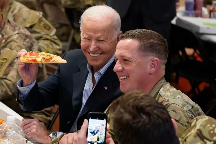 President Joe Biden holds a piece of pizza as he posed for a photo during a visit with members of the 82nd Airborne Division at the G2A Arena, Friday, March 25, 2022, in Jasionka, Poland.